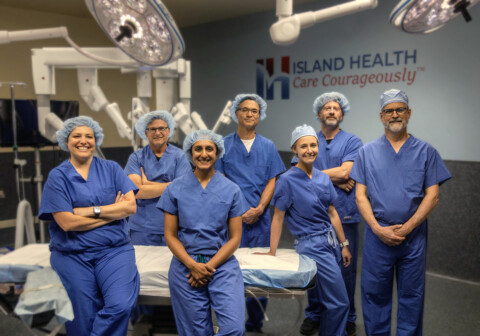 Island Health Surgeons gathered around the da Vinci 5 Surgical Robot.