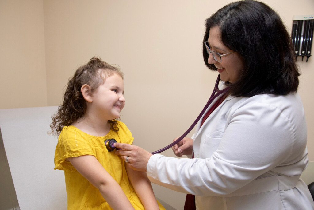 Pediatrician checking the heart of a little girl wearing a yellow dress.