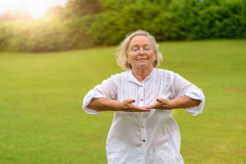 Woman standing outside in a green field taking a deep breath.