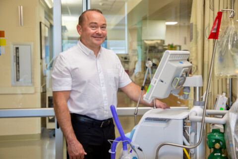 Man in a white shirt standing in front of medical equipment, smiling.