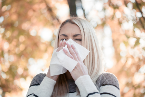 Woman outside in the fall sneezing into a tissue.