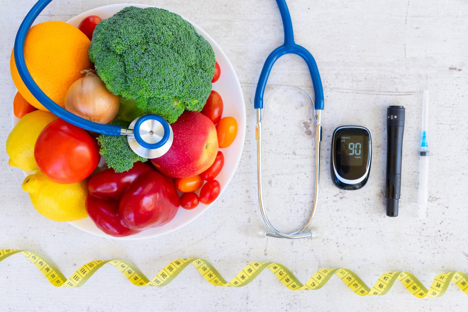 A plate of fruit and vegetables next to a stethoscope, blood sugar monitor, and other tools used for people with diabetes.