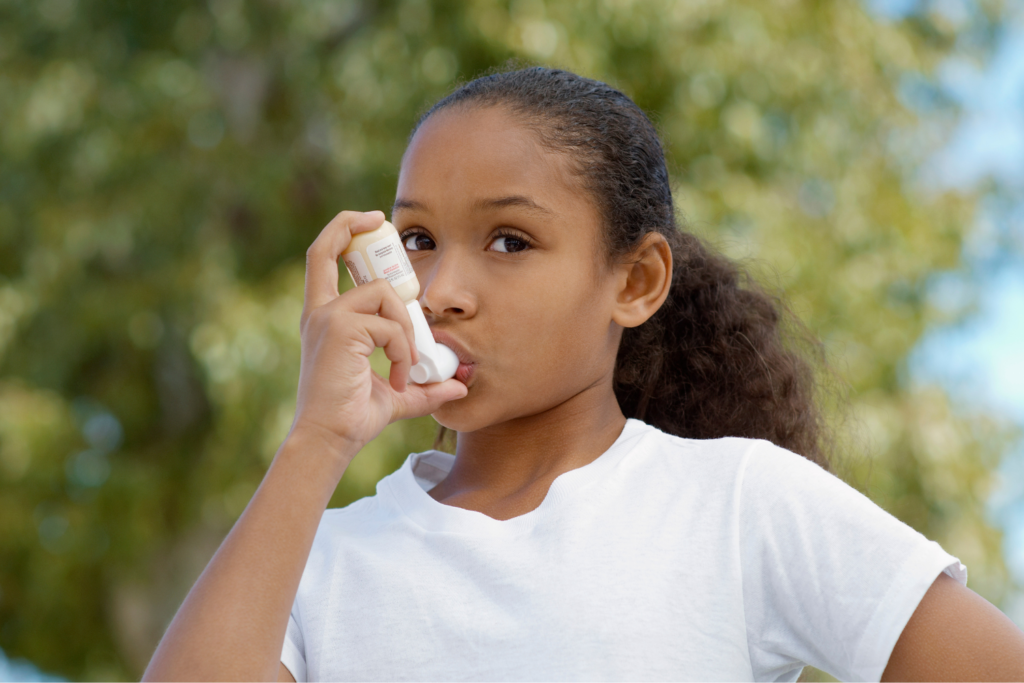 Young girl standing outside using an inhaler.