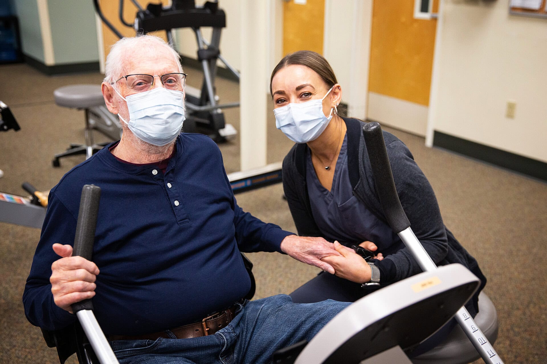 A patient sits on a recumbent exercise bike next to the director of pulmonary rehabilitation at Island Health.