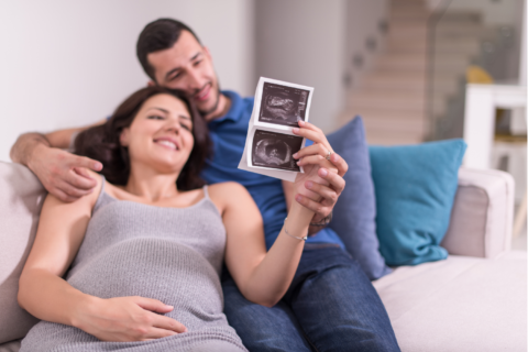 Happy, expecting couple looking at a sonogram while laying on a couch.