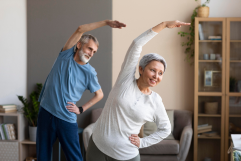 older man in blue shirt and older woman in white shirt smiling and doing a yoga pose