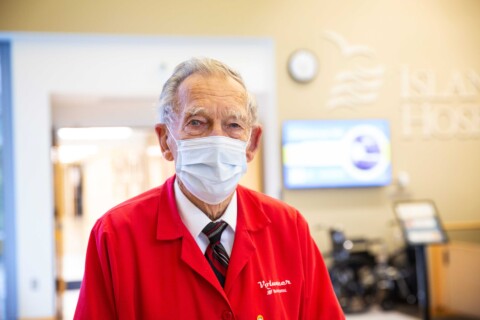 Senior male hospital volunteer wearing mask and volunteer red jacket.