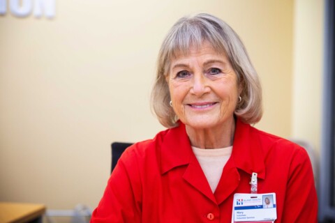 Smiling female Surgery Desk volunteer in red volunteer jacket.