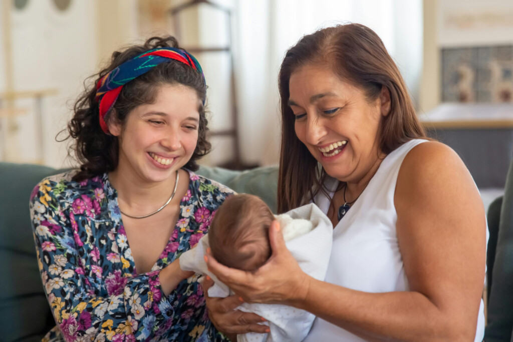Three generations of women sitting on a couch holding a new baby.