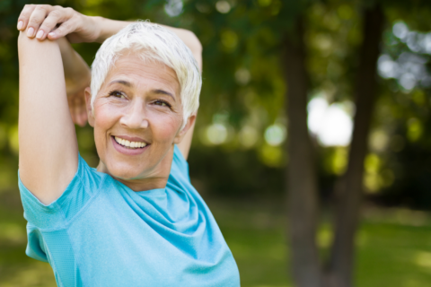 Older woman smiling while stretching in the park.