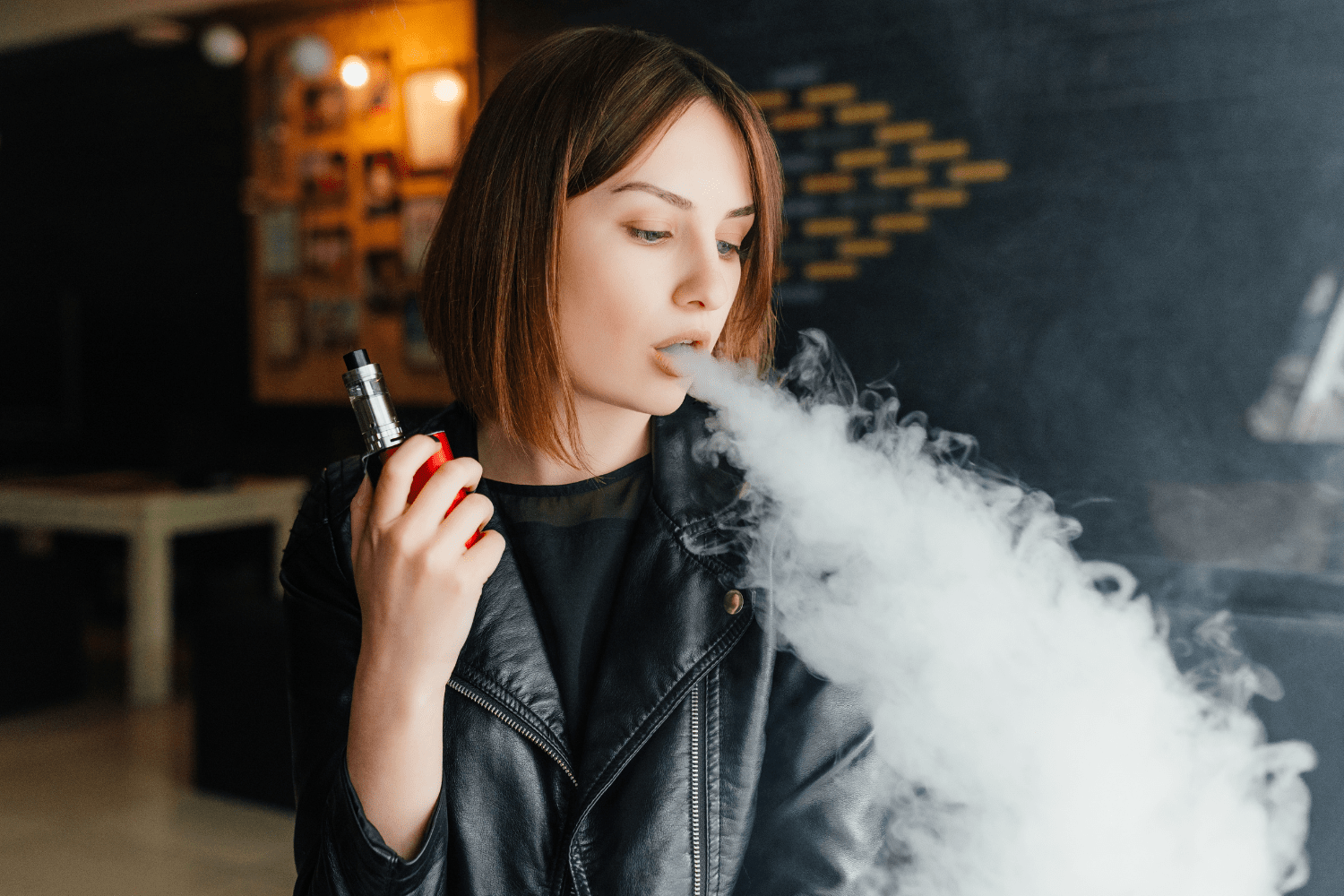Girl dressed in black leather jacket vaping from a red vape.