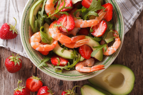 Bowl of mixed green salad with shrimp, strawberries and avocados.