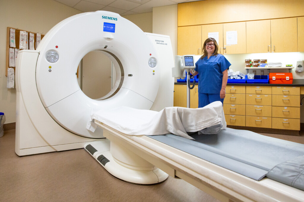 Island Health employee standing next to the CT machine