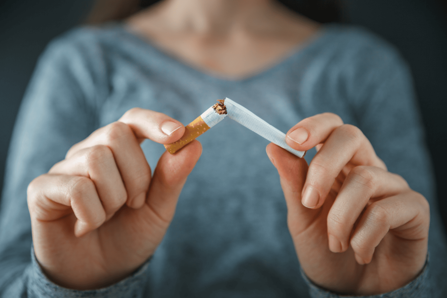 Image of woman in a blue shirt breaking a cigarette apart.