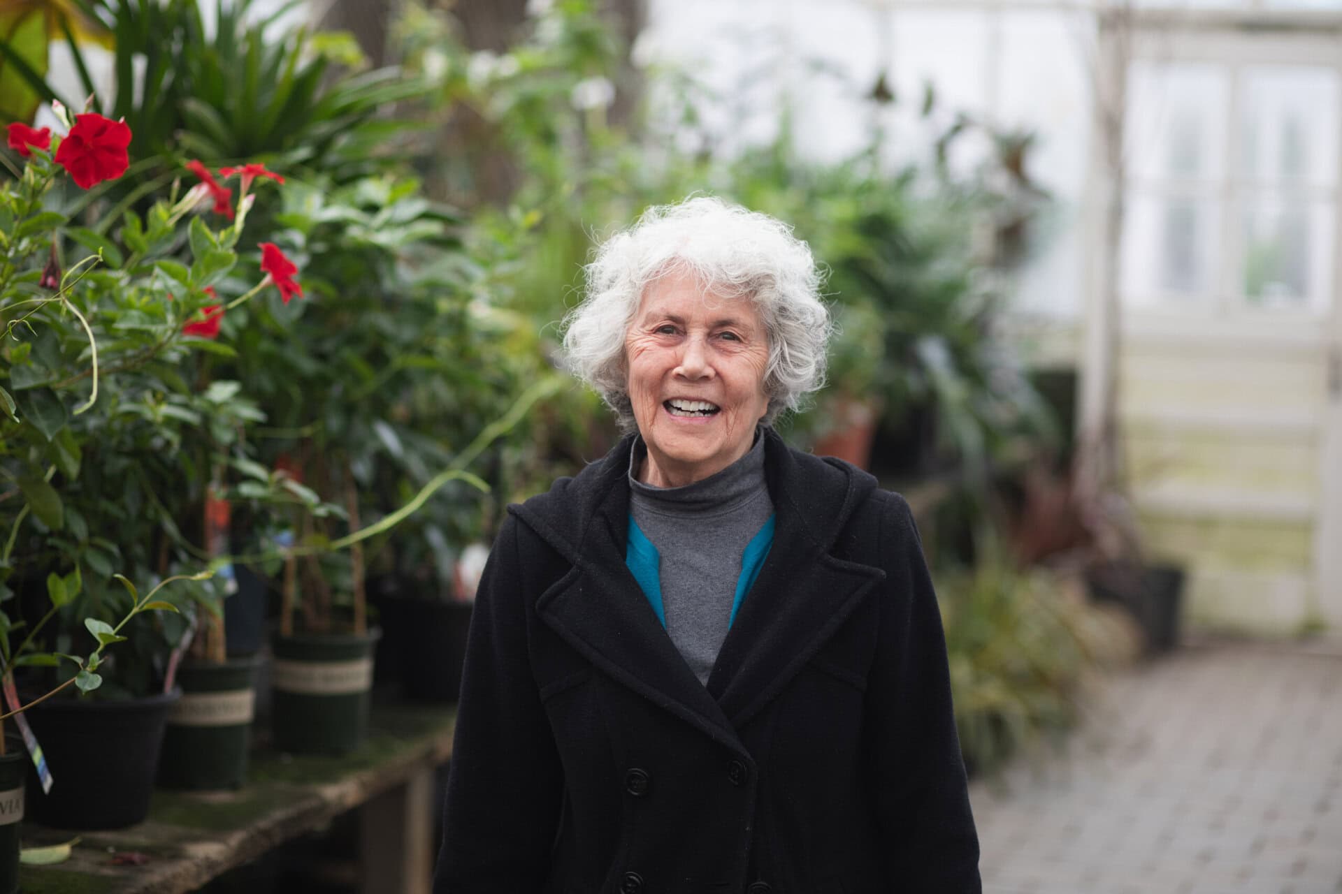 Woman standing in a greenhouse next to plants and flowers.