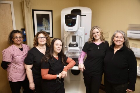 Five mammogram techs in scrubs stand in front of mammography equipment.