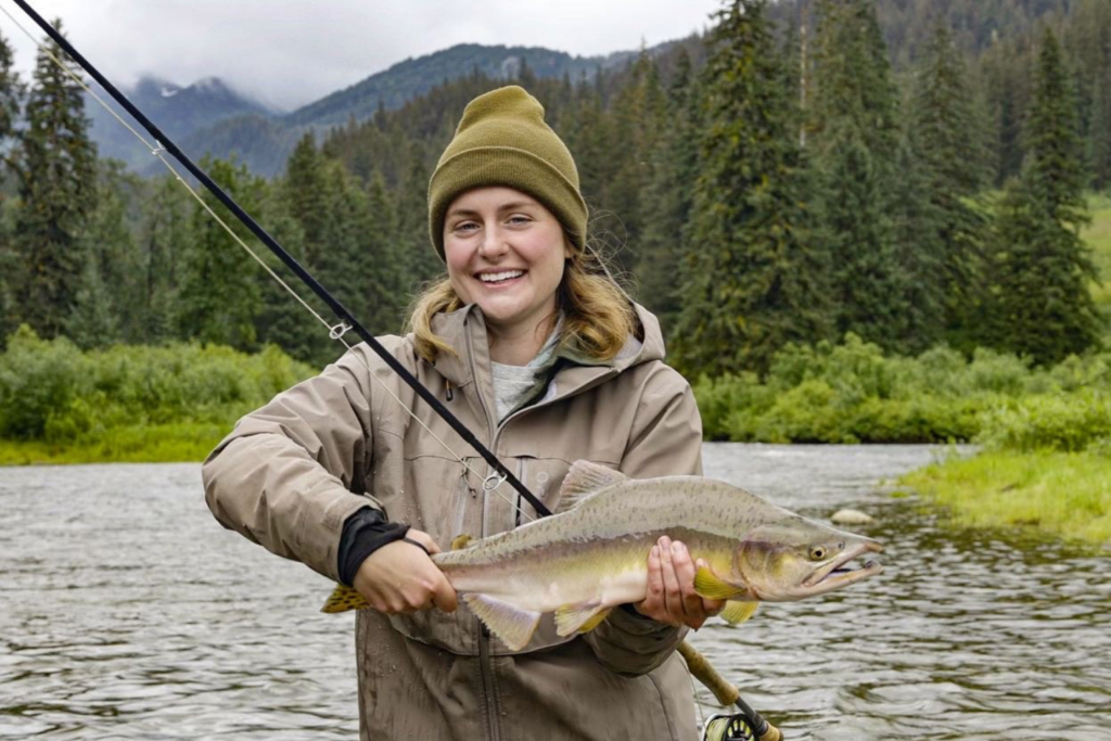 Family Medicine Provider Dr. Brittany Whitaker standing by a river, holding a fishing rod and fish she caught.
