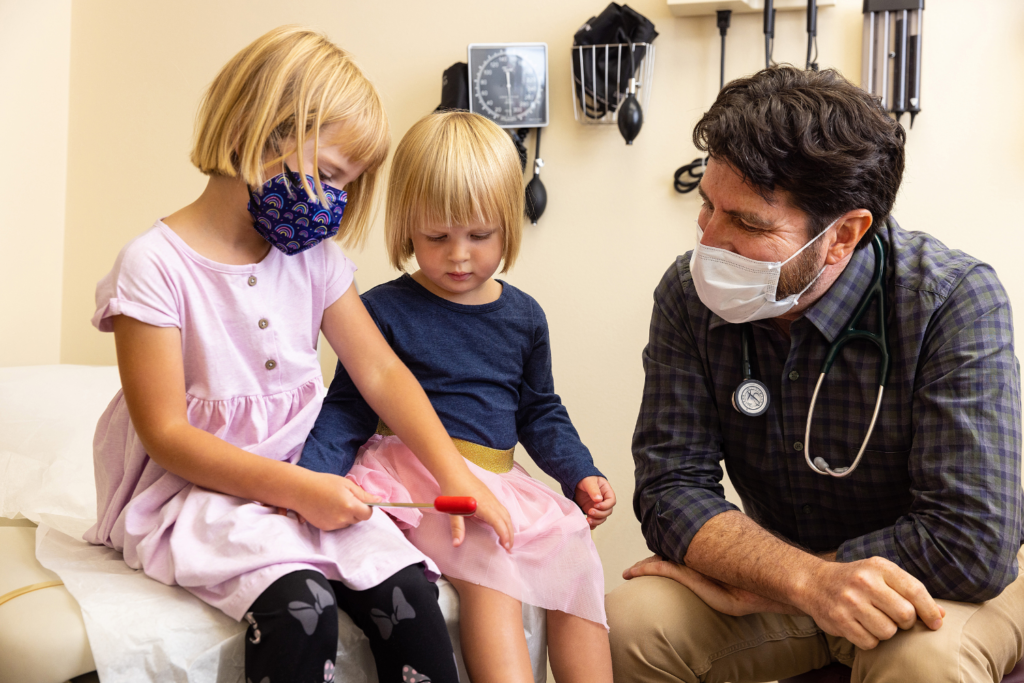 Pediatrician with two, young, female patients in clinic room.