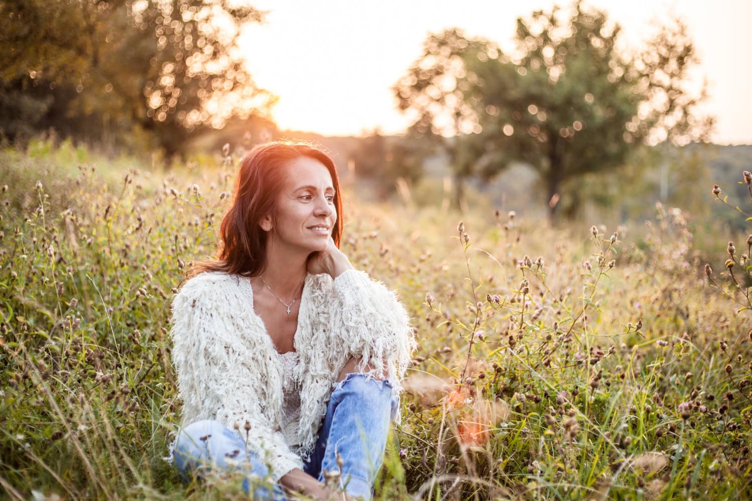 woman in white sweater sitting in a field with flowers