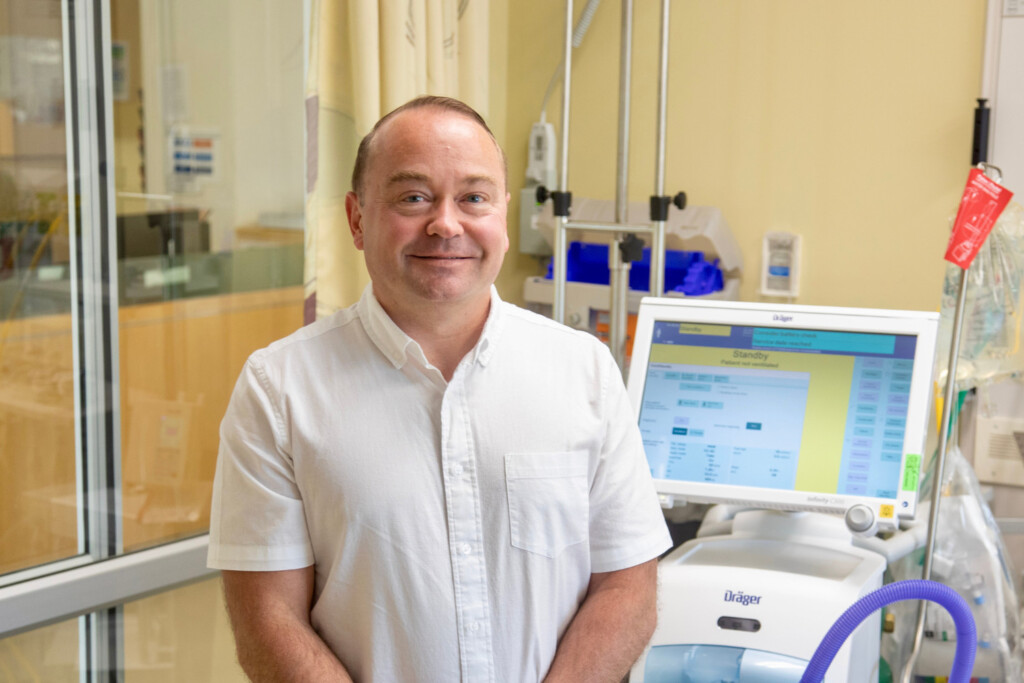 Respiratory Therapist Jeffrey Freeland standing in front of a ventilator in a patient room.