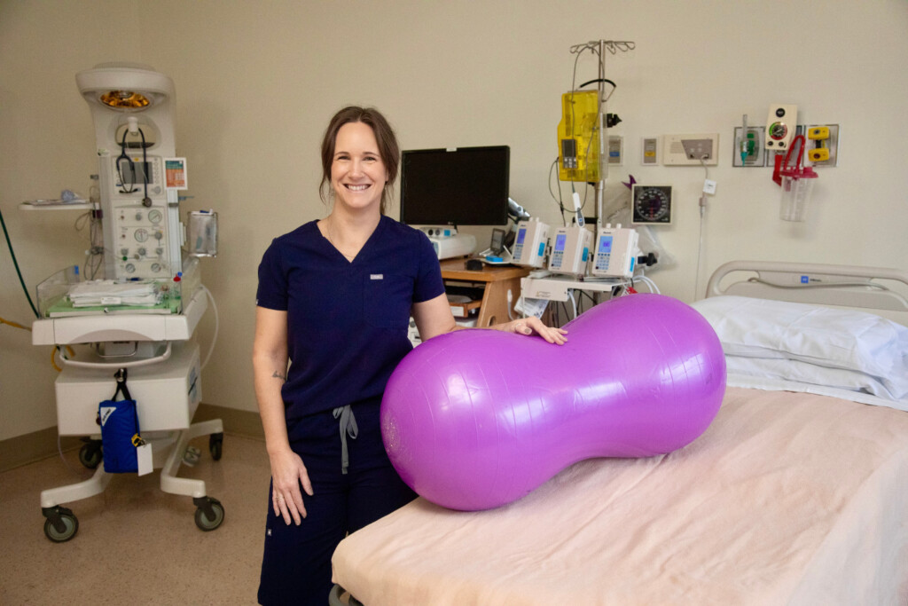 Nurse standing in a delivery room with a peanut ball on the bed and smiling.