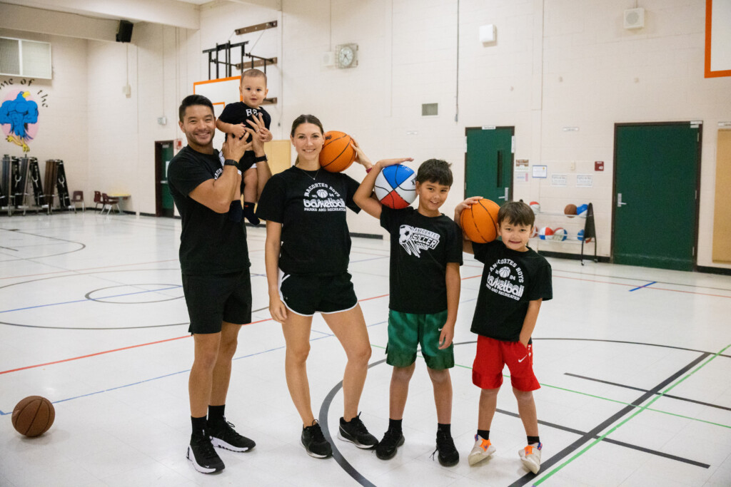 Family in a gymnasium holding basketballs and smiling.