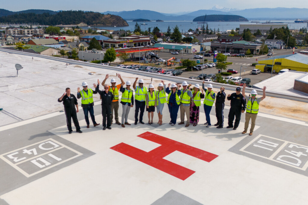 Island Health leaders, community partners and government officials standing on the rooftop helipad waving.