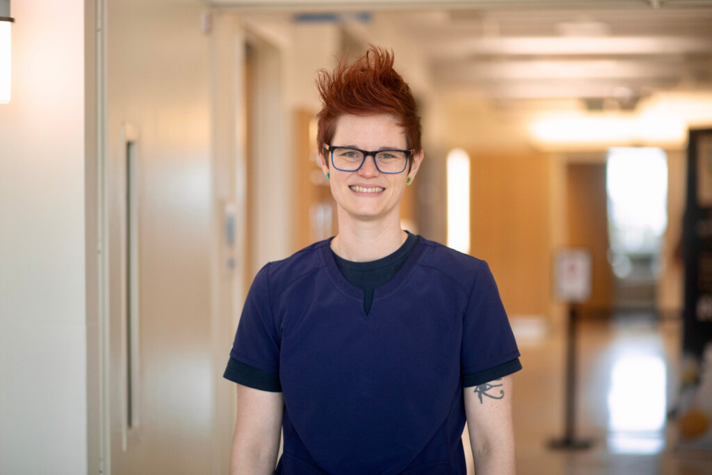 Woman with red hair standing in a clinical hallway smiling.