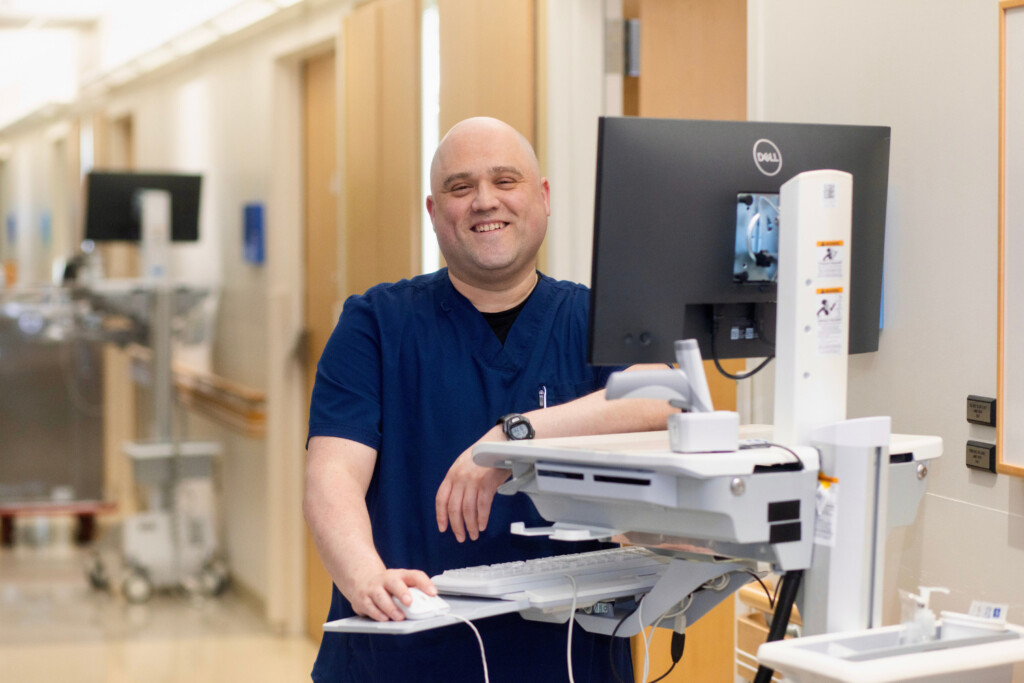 Nurse standing next to mobile computer smiling.