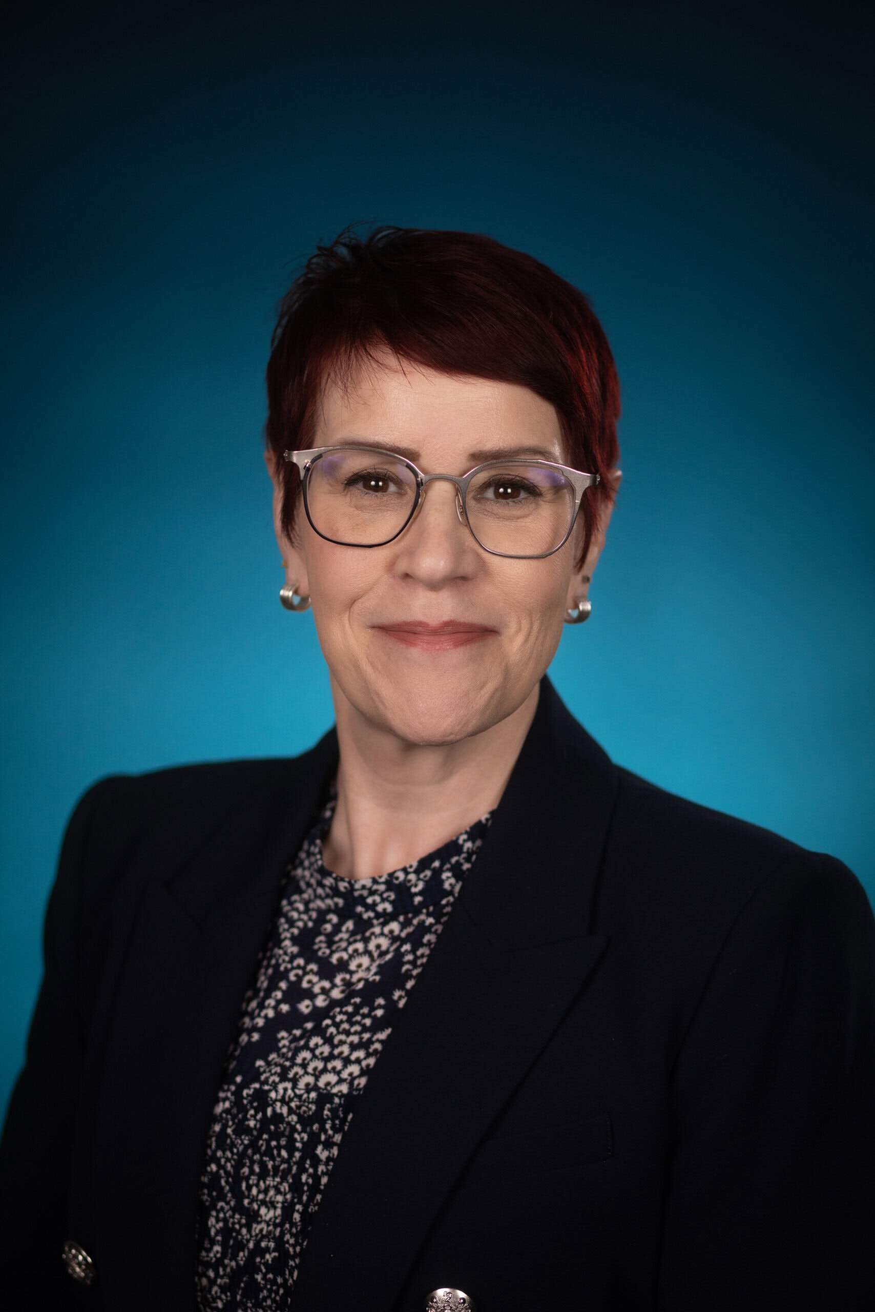 Woman with short red hair and glasses smiling at the camera.