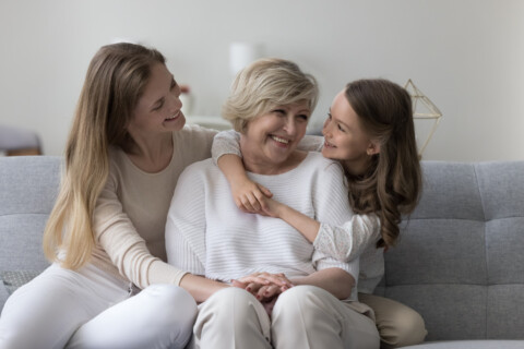 Three generations of women sitting on a couch smiling at each other.
