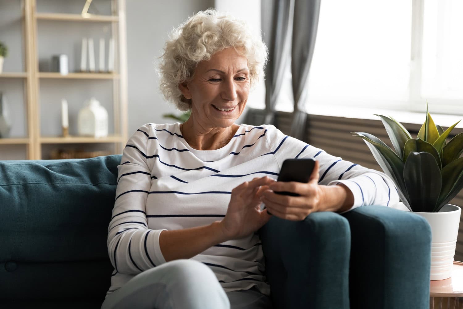 blog size graphics – 2025-10-28T102543.032 Older woman sitting on her couch and looking at something on her phone.
