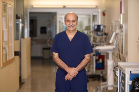 Cardiologist Rajesh Bhola, MD standing in hallway smiling.