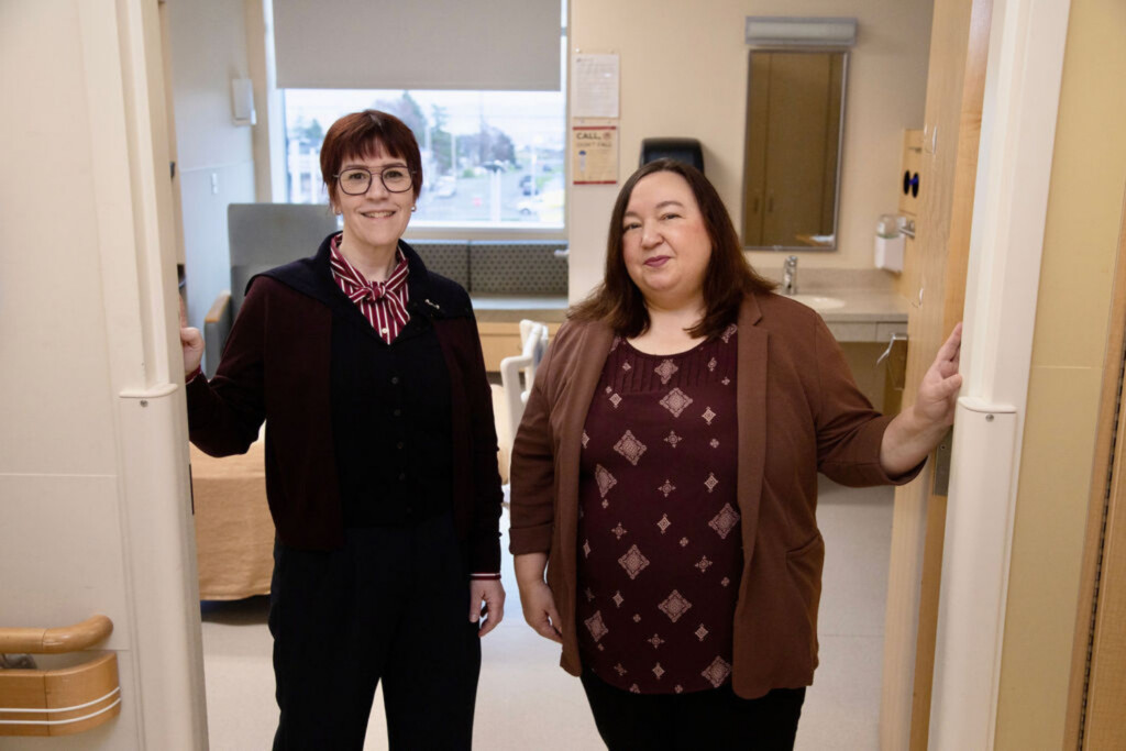 Two women standing in the doorway of a hospital room, smiling.