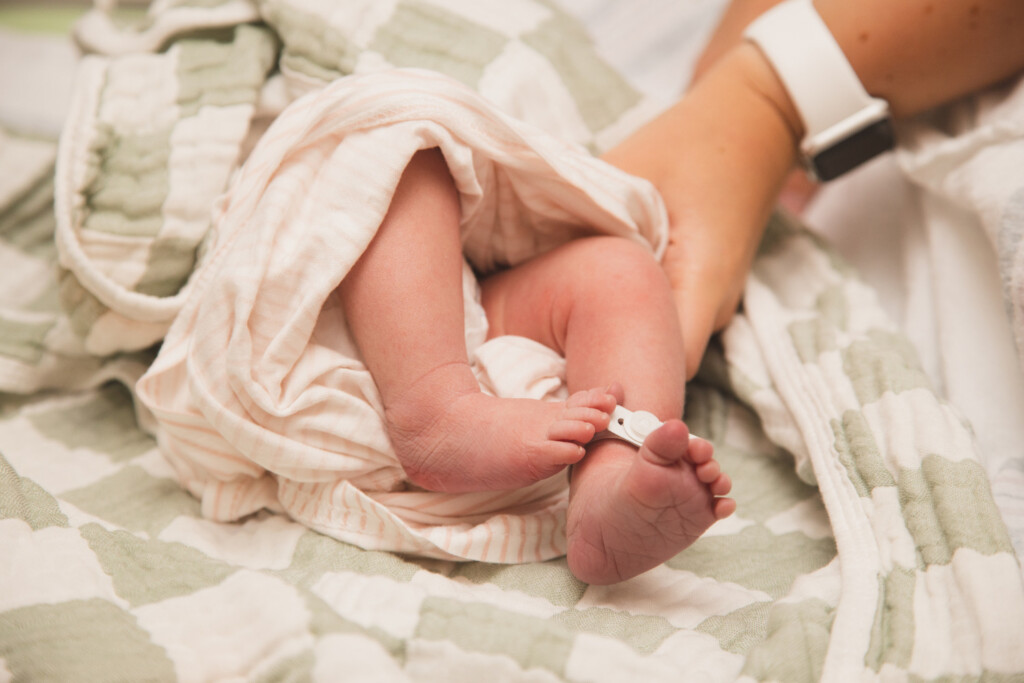 Newborn baby feet swaddled in a blanket with an adult hand cradling the baby.