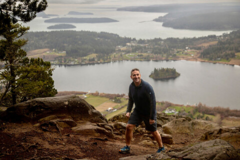 Man hiking at Mt. Erie, with Campbell Lake and surrounding San Juan Islands in the background