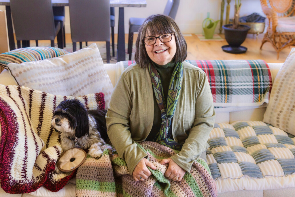 Woman sitting on a couch with a blanket next to her dog.