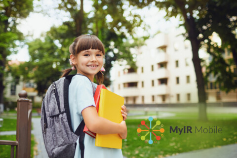 Young girl walking into school with a backpack and holding folders.