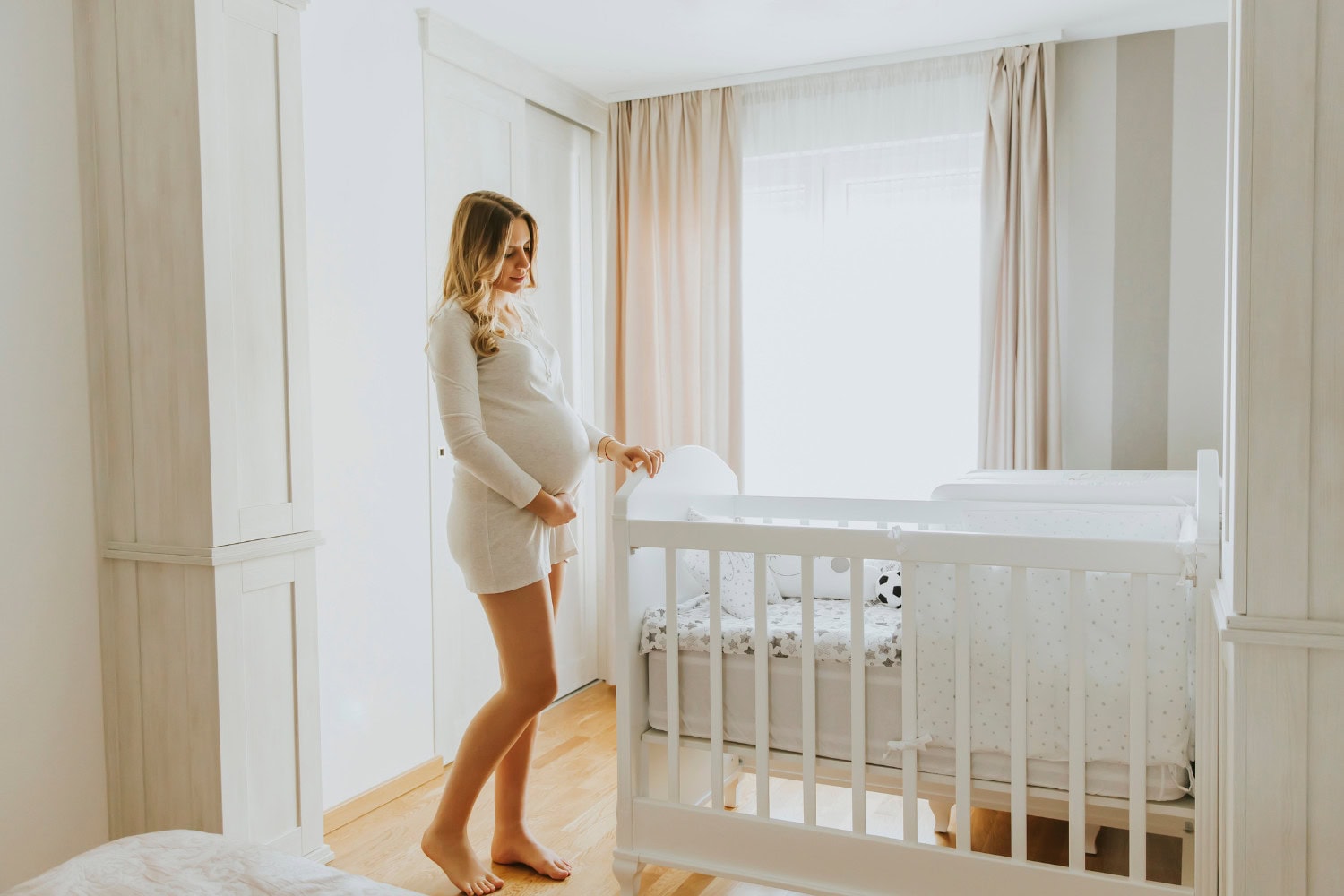 Expectant mother standing in nursery looking at the crib.