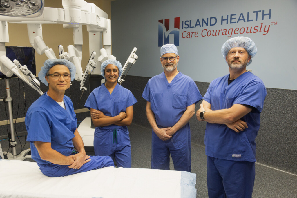 Island General Surgery & Gastroenterology surgeons standing by the da Vinci 5 surgical robot, wearing scrubs.