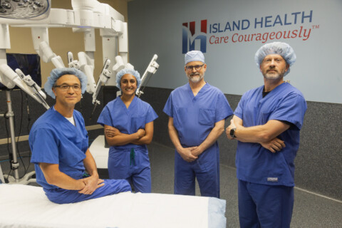 Island General Surgery & Gastroenterology surgeons standing by the da Vinci 5 surgical robot, wearing scrubs.