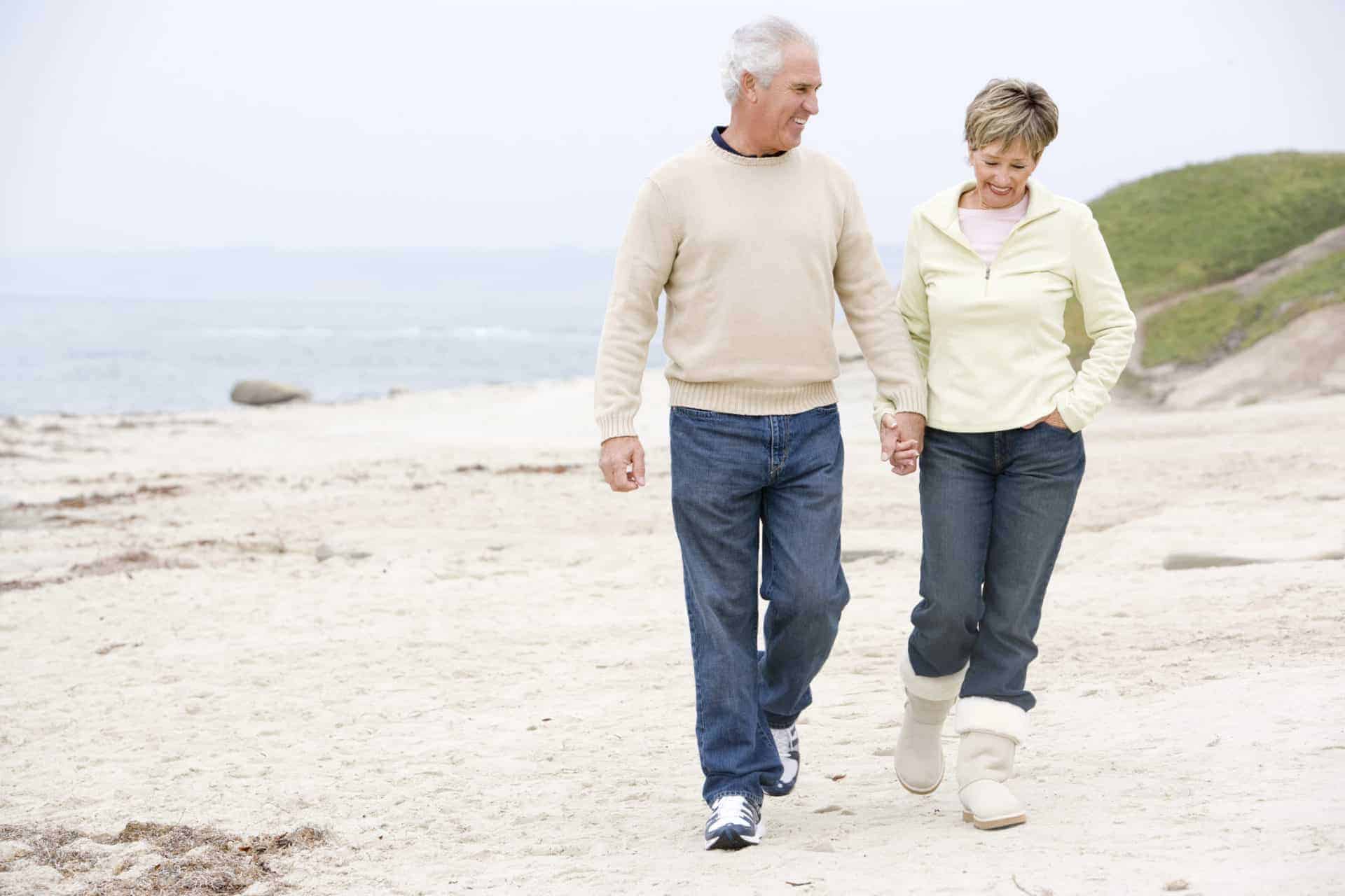 A mature couple walking on a beach holding hands.